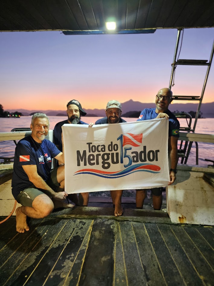 Equipe e membros da Toca do Mergulhador reunidos no barco com a bandeira do clube